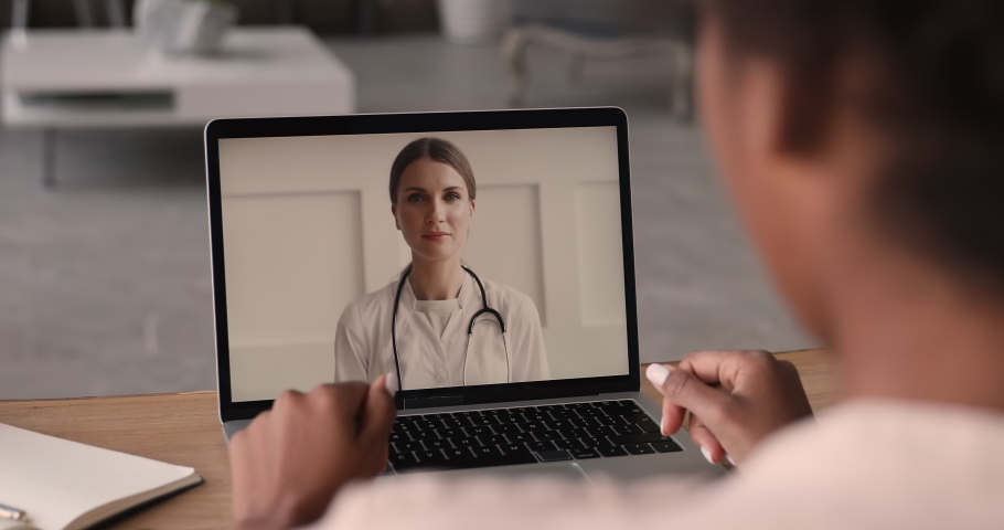 Female doctor videoconferencing to young african woman by videocall, consulting about corona virus pandemic, laptop screen view over patient shoulder. Medical on-line conference, quarantine concept Royalty-Free Stock Footage #1065238153