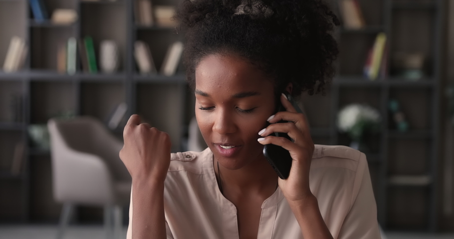 Attractive young african woman talk on phone sit at workplace enjoy formal or personal conversation. Mixed-race female holding modern smartphone solve business remotely, having pleasant blab concept Royalty-Free Stock Footage #1065238213