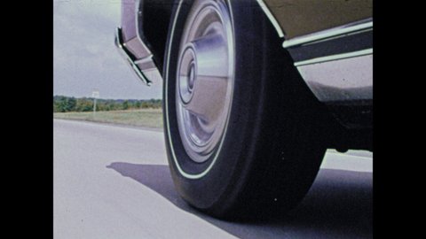 1970s: Close-up car tires driving on road. Brake lights. Flashing yellow traffic light. Yellow and white road markings. Montage of road signs. Stop sign. Car screeches to stop. Car tires turning.