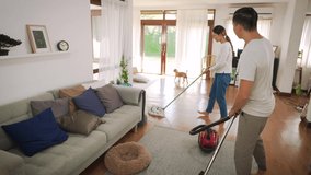 Happy young couple of woman cleaning carpet with vacuum cleaner machine and man mopping the floor at modern home - 4k Video Footage