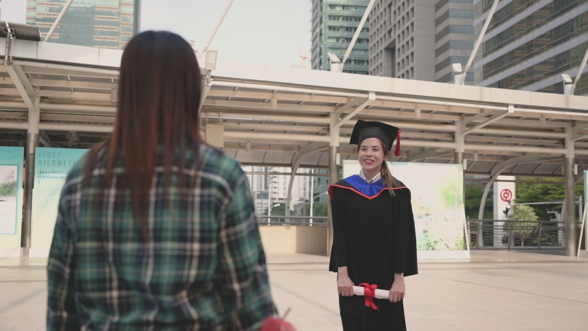 Happy beautiful young woman in graduation gowns with holding diploma are hugged mother by love and proud in city on outdoors. Asian mom embraces daughter with joy on graduation day and successful. Royalty-Free Stock Footage #1065251764