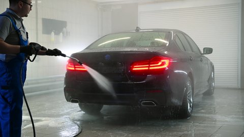 Man spraying water from high pressure washer to wash a car at car care shop.