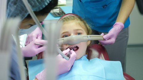 Modern dentistry. Little girl getting Inhalation Sedation while teeth treatment in dental clinic. Doctor putting on Laghing gas mask to relax and calm young overactive patient down. 4 k