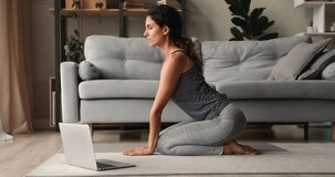 30s woman wear grey comfy activewear do yoga in living room, stretches neck makes back bend perform asanas at home, watch online training repeat exercises, boost flexibility, sporty lifestyle concept