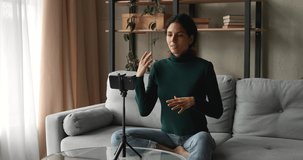 Woman record new educational videovlog for channel using smart phone sit on sofa at home, put device on tripod female film vlog lead on-line live stream. Modern technology usage, video event concept
