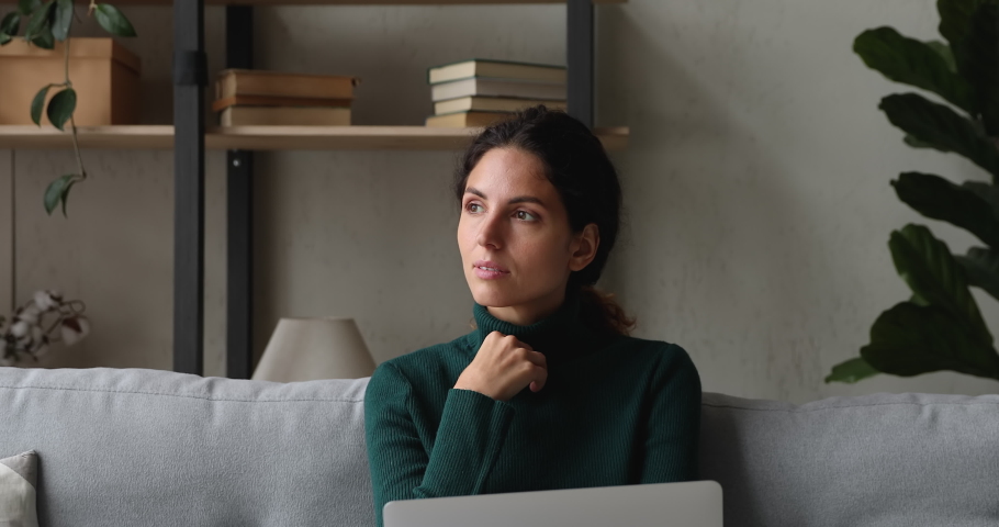 Thoughtful young woman sitting on couch with laptop search of inspiration, dreaming looking into distance, lost in thoughts. Blogger writing article, female do creative telecommute work online concept Royalty-Free Stock Footage #1065265963