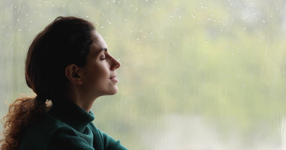 Close up profile face calm woman sit on windowsill near window closed eyes enjoy fresh air, do breathing exercise, relaxing indoor, rainy weather outside. No stress, meditation, anxiety relief concept Royalty-Free Stock Footage #1065266035