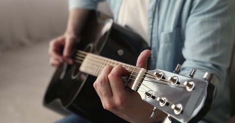Close up view unrecognizable man holding playing acoustic guitar seated at home alone. Concept of self-taught activity, favourite hobby, pastime, talented person compose music uses string instrument