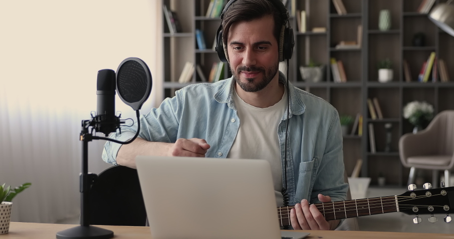 Young man sit indoor greeting learner start videoconference call on laptop play acoustic guitar, on-line teacher wear headphones teaches remotely play string instrument. Online tutoring, hobby concept Royalty-Free Stock Footage #1065266323