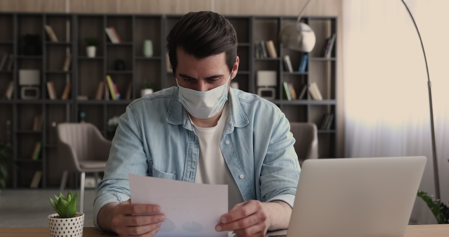 Employee in protective disposable facemask sit at workplace use laptop prepare report, hold document paper makes presentation, analyzing statistics sales data. Analysis, strategizing, planning concept Royalty-Free Stock Footage #1065266560