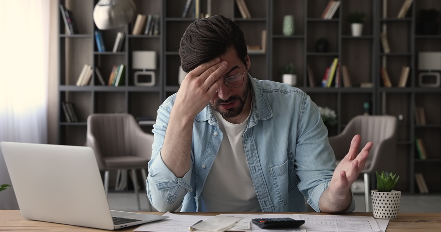 Frustrated man sit at desk with paper bills and laptop, calculates finances, feeling stressed about bank loan payment, thinking of unpaid high taxes, financial problem, money lack, bankruptcy concept | Shutterstock HD Video #1065266566
