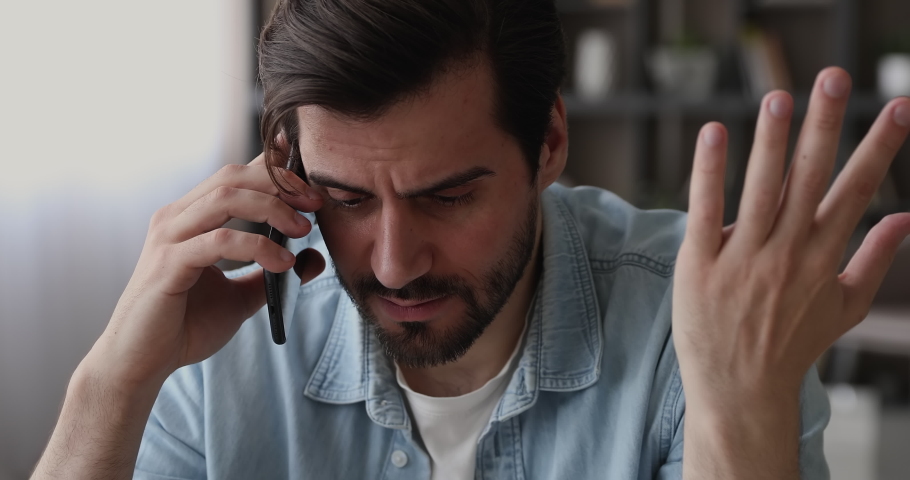Young man sit indoor talking on smartphone hearing bad news, office employee holding cellphone listen client complaints during phone conversation looking disappointed feel stressed, close up face view Royalty-Free Stock Footage #1065266686