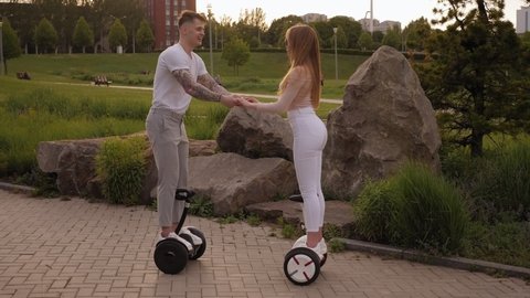 A young sports couple rides a gyro scooter and kissed in a beautiful Park in the summer at sunset. Happy man and woman riding on the hoverboard. Active lifestyle.