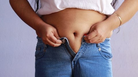 mid section of an Indian woman with belly fat wearing blue jeans