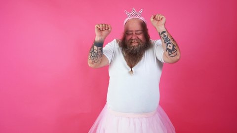 Cinematic footage of a funny man with hispter beard acting on a colored background. Middle aged person wearing a ballerina costume dancing and having fun