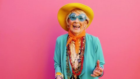 Cinematic footage of an old italian woman having fun on colored background. Happy grandmother with vibrant colored fashion looks