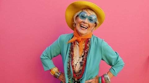 Cinematic footage of an old italian woman having fun on colored background. Happy grandmother with vibrant colored fashion looks