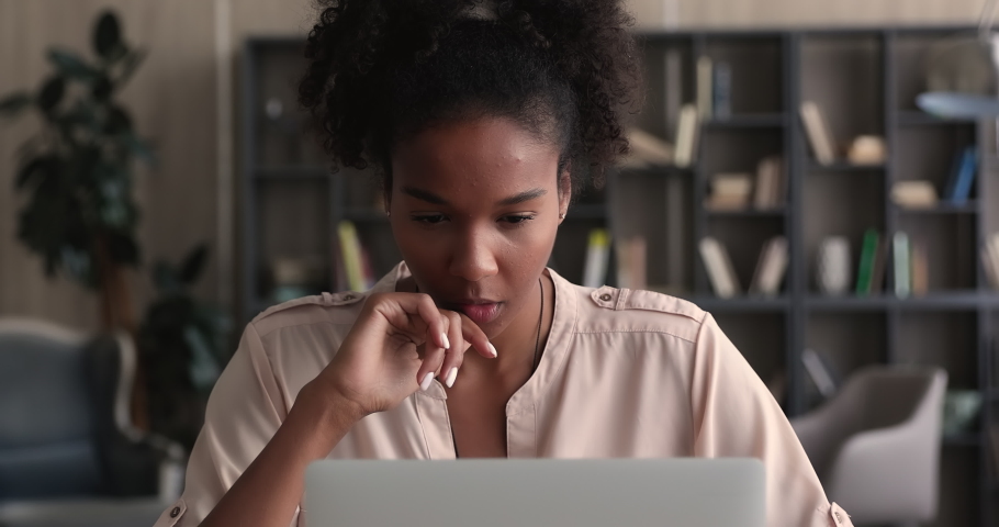 Focused african woman sit at desk looking at laptop learn new app, work on research project online on computer, makes remote telecommute task, thinking of problem solution, watch webinar or read email Royalty-Free Stock Footage #1065279406