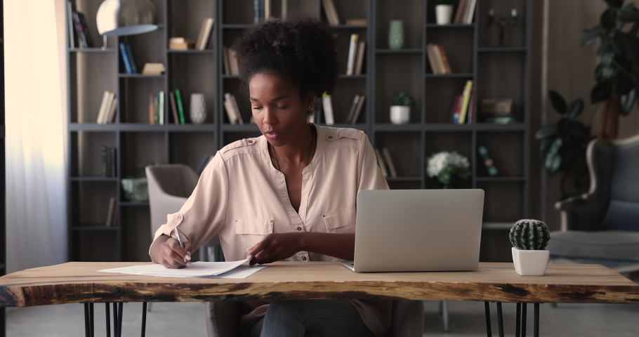 African ethnicity female manager prepare financial report making presentation writes notes or corrections do paperwork seated at modern workplace in office alone. Banking, management, finances concept Royalty-Free Stock Footage #1065279418