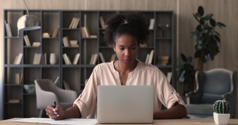 African woman working on financial paperwork seated at workplace using laptop app looks concentrated while makes task, prepare, check report having fruitful workday. Student learning process concept Royalty-Free Stock Footage #1065279421