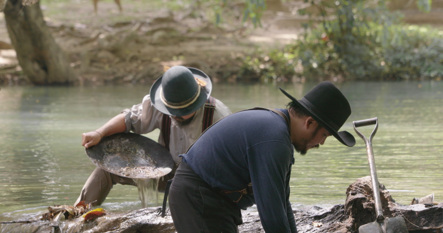 Gold digger wearing on cowboy hat standing tin the water one using shovel digging soil from water pouring to gold panning to refining the gold metal particles  