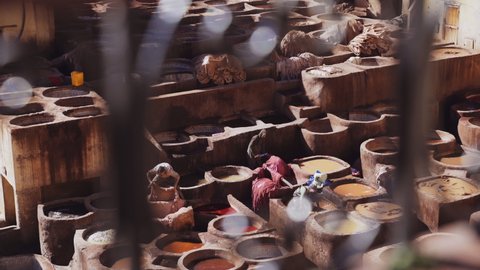 FEZ, MOROCCO - OCTOBER 2020: Elevated Handheld Panning Wide Shot Of Workers Standing In The Dye Pots, Cutting And Preparing Leather In The Chouara Tannery, Fez, Morocco
