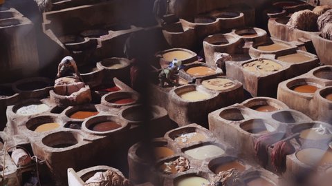 FEZ, MOROCCO - OCTOBER 2020: Elevated Slow Motion Tracking Wide Shot Of People Working In The Chouara Tannery, Tanning Leather From Large Pots Of Dye, Fez, Morocco