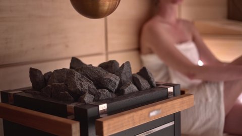 Woman relaxing and sweating in hot sauna. Real, authentic sauna moment. Focus on sauna stove and stone.