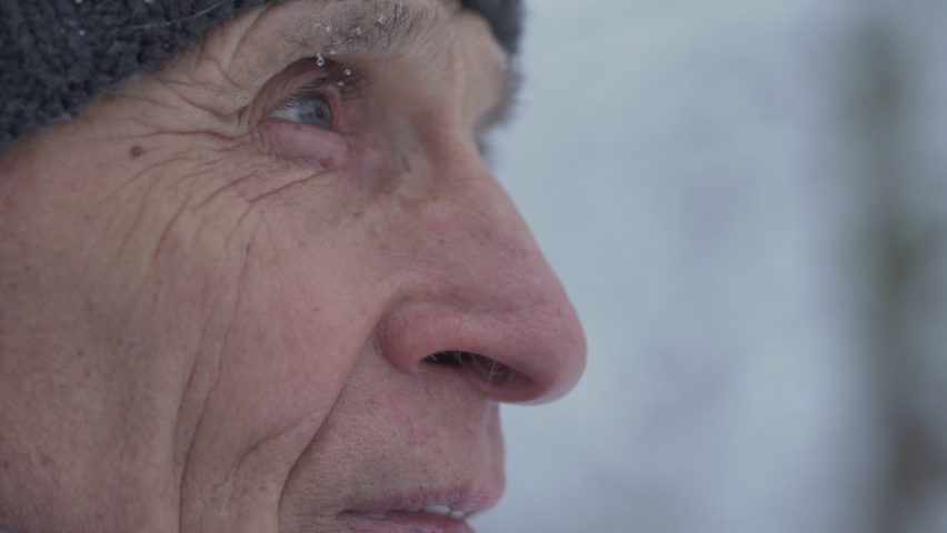 Close side view of wrinkled face of old man stands outdoor in snowy blizzard. Concept pensive and wisdom.
