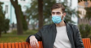 Slow Motion Young businessman in medical protective mask sits on the bench in public garden, then he takes off his face mask and puts it in his pocket. Cinema 4K 60fps video