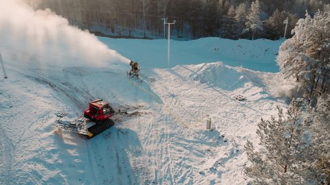 Aerial view snow cannon stands on a snowy mountain in the winter and works by producing a column of snow on the background of beautiful pine trees, and the ski slopes. Ski. Winter sport. Snow-making