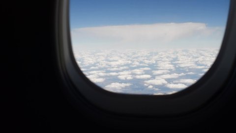 Airplane window opening by hand with white clouds outside aircraft.
