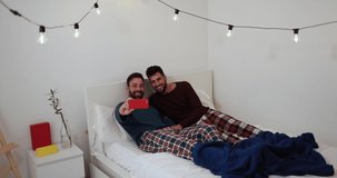 Gay men couple fun on a video call in the morning in bedroom while wearing pyjama