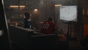 Two friends playing hockey sport video game inside garage hideout, scoring and celebrating. TV screen is blurred. Shot with 2x anamorphic lens