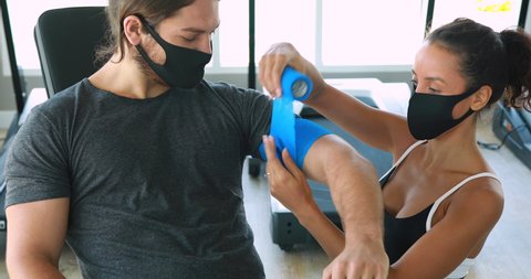 Hispanic woman physiotherapist apply neuromuscular bandage to her patient at gym training professional clinic.