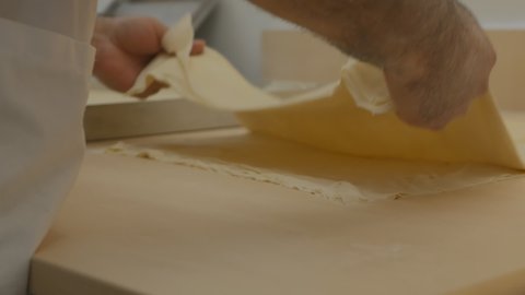 Turkish pastry chef man rolls out many layers of thin dough for baklava with a rolling pin. The baker flattens the layers, rolls them out many times. Close-up of a pastry chef's hand