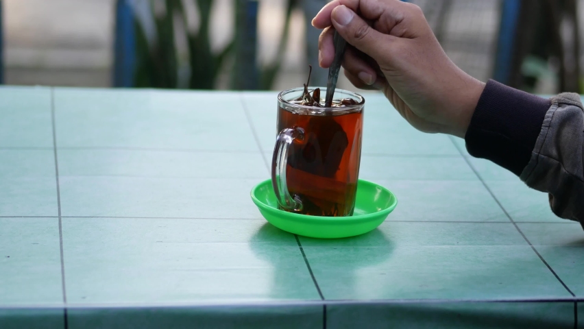 an Indonesian man stirring warm wedang uwuh in a glass. wedang uwuh. made of ginger, secang, cloves, cardamom, dried cinnamon. Indonesian traditional drink.