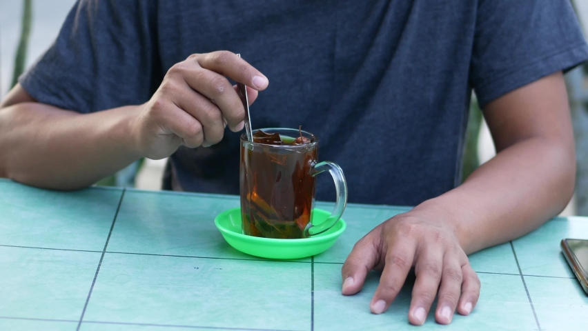 an Indonesian man stirring warm wedang uwuh in a glass. wedang uwuh made of ginger, secang, cloves, cardamom, dried cinnamon. Indonesian traditional drink.