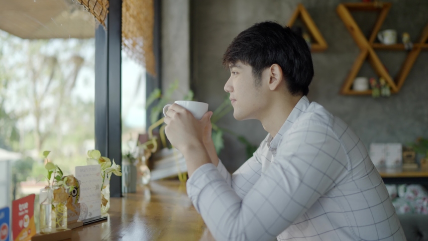 Slow Motion: A beautiful Asian man wearing a white shirt is drinking coffee in the store. And beaming Royalty-Free Stock Footage #1065323857