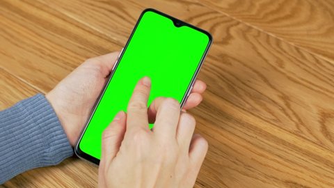 Close-Up Of A Woman Using A Phone Touches Her Fingers on a Green Background Green Screen Chroma Key Smartphone. Close-up of the Phone Screen and a Woman's Hand. Blogging, Internet, Content Viewing.