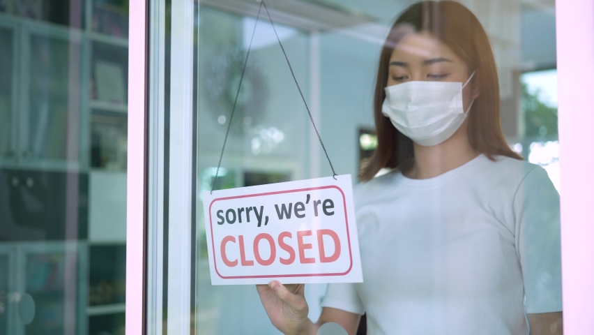 Woman with sad emotion wearing face mask turning a sign from open to closed on a door shop. Small shop closed after covid-19 quarantine lockdown. | Shutterstock HD Video #1065327325