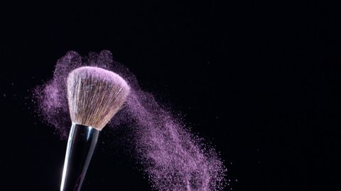 Makeup brush shudders and creates a swirl of fine particles of pink powder against a black background, slow motion, 300fps.