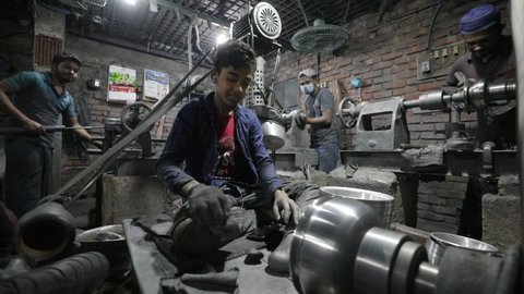 DHAKA, BANGLADESH - JANUARY 10, 2021: A young underaged kid is doing child labour in a dark sweatshop factory without any occupational health and safety precautions
