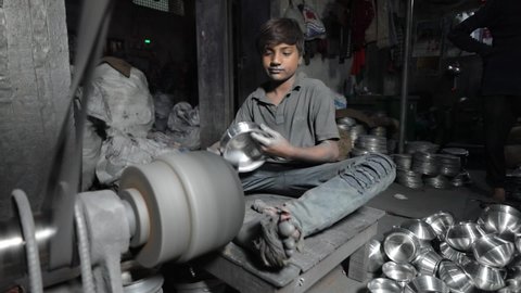 DHAKA, BANGLADESH - JANUARY 10, 2021: A young underaged kid is doing child labour in a dark sweatshop factory without any occupational health and safety precautions