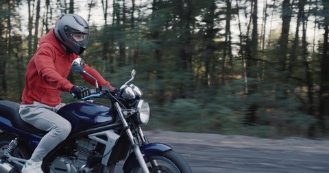 Young motorcyclist quickly rides along the road along the forest