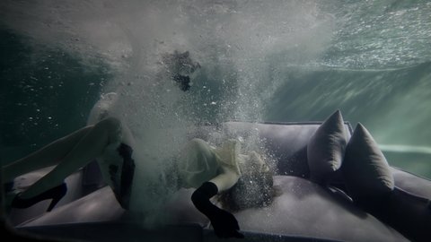 woman is plunging inside pool and lying on couch on bottom, underwater slow motion shot