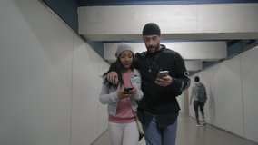 A young interracial couple walking embraced in a subway corridor. Young black woman and young caucasian talking about something on her smart phone. - Powered by Shutterstock - Get 15% off with code: PIKWIZARD15