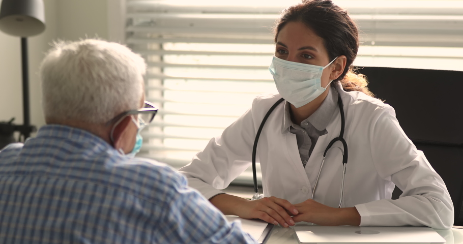 Serious confident cardiologist wear white coat surgical face mask talk to older patient, explain prescription, heart disease treatment. Geriatrics, medical insurance services for aged people concept Royalty-Free Stock Footage #1065341392