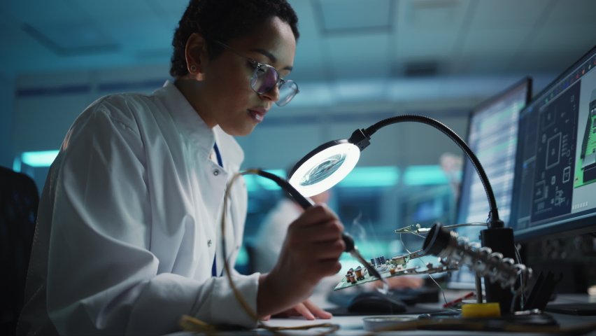 Modern Electronics Facility: Beautiful Black Female Scientist, Engineer Does Printed Curcuit Motherboard Soldering. Does Design, Development of Industrial PCB, Silicon Microchips, Semiconductors Royalty-Free Stock Footage #1065341740