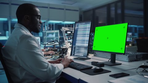 Modern Electronics Facility: Scientist, Engineer Works on Green Chroma Key Screen Computer. Design, Development of Industrial PCB, Silicon Microchips, Semiconductors, Telecommunications Equipment